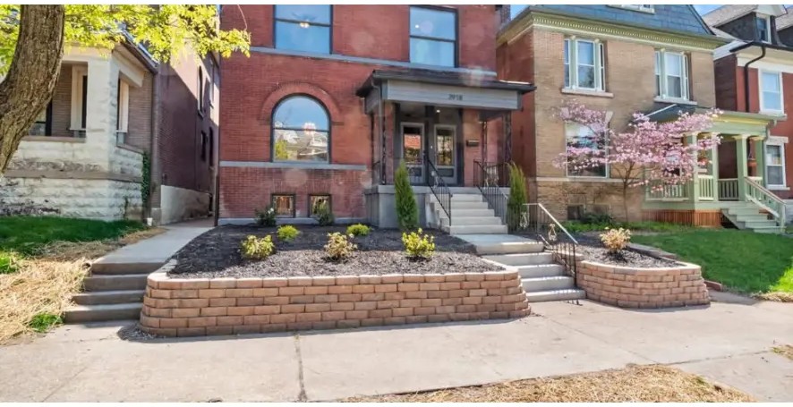 Red brick home with arched window, terraced brick planters and concrete steps