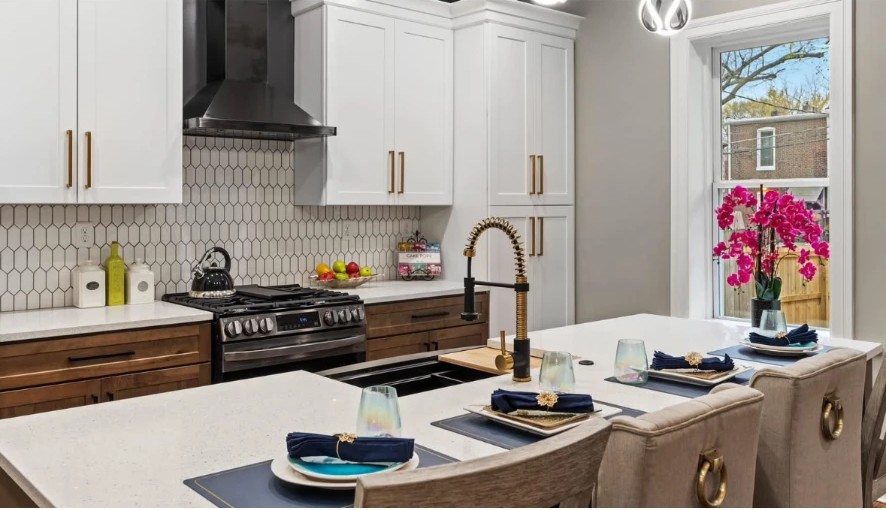 Kitchen island with place settings, brass faucet and pink orchid beside a tall window