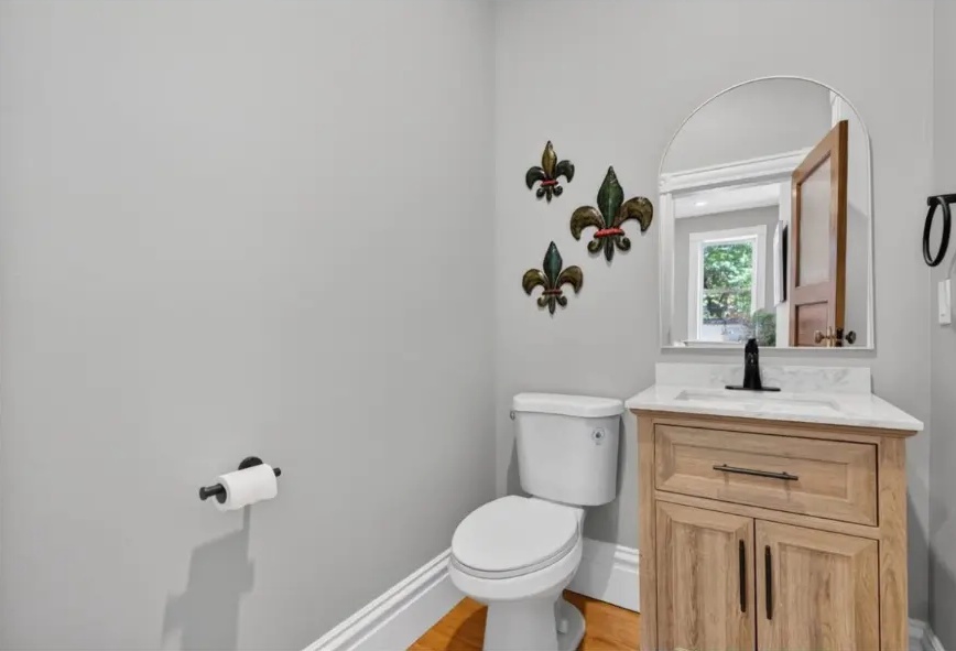 Powder room with wood vanity, light countertop, black faucet and arched mirror
