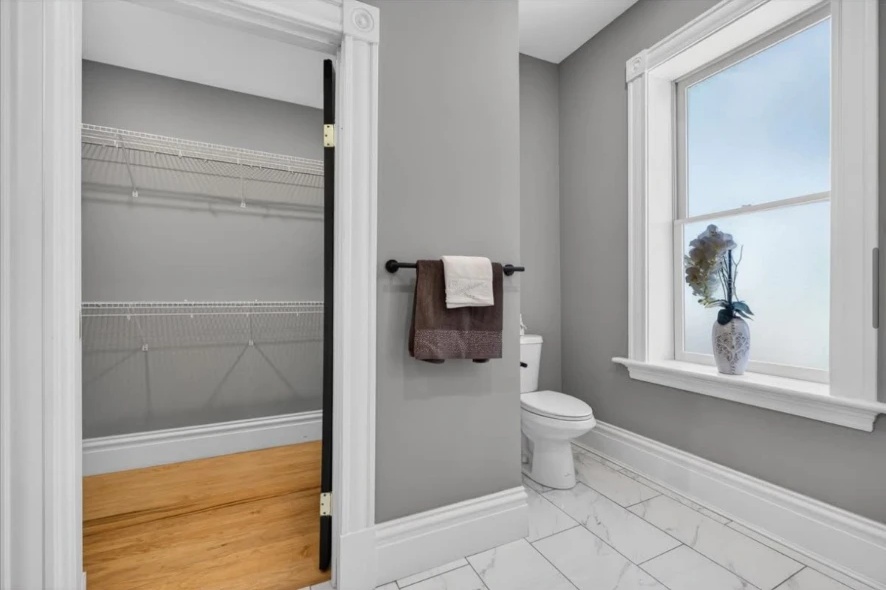 Bathroom corner with white-trimmed window, toilet, towel rail and adjoining wood-floored closet