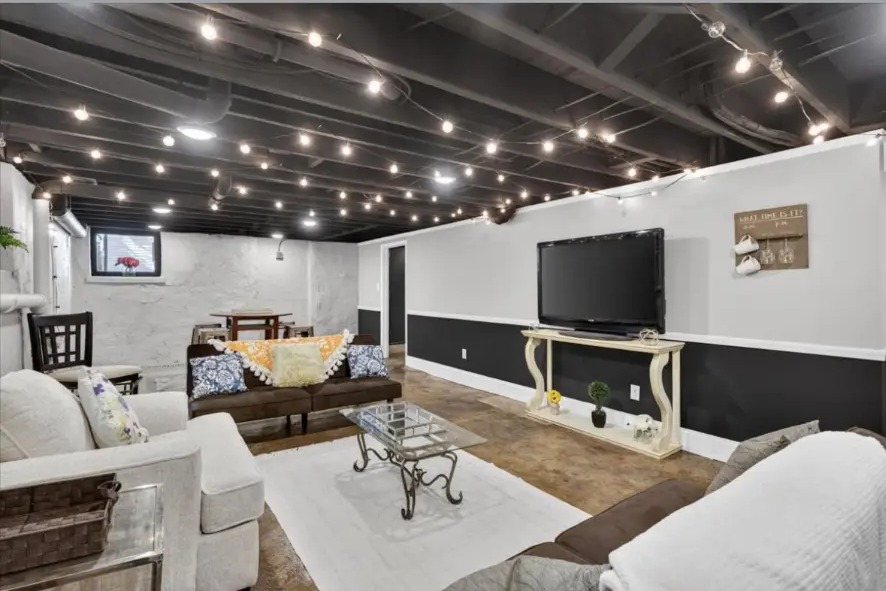 Basement living area with wall-mounted TV, console table, sofas and string lights