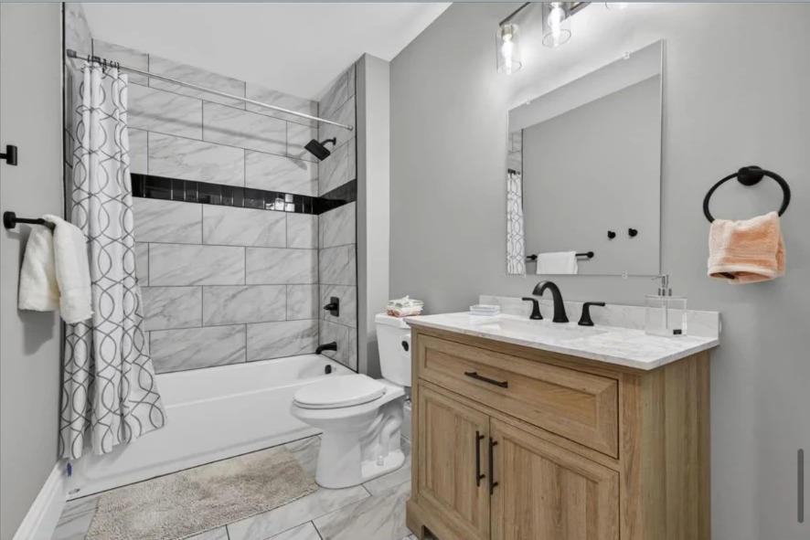 Bathroom with tiled tub surround, wood vanity, black fixtures and mirror