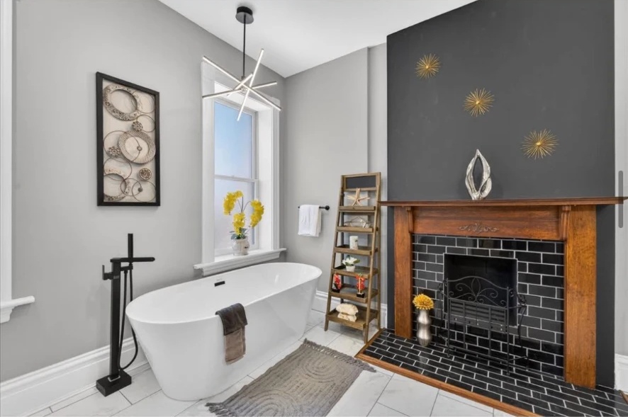White freestanding bathtub beside a wood mantel and black tiled fireplace