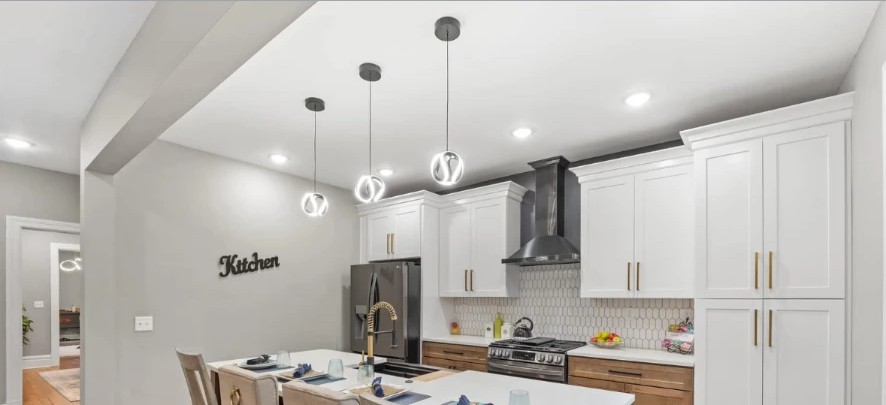 Kitchen with white cabinetry, brass hardware, vaulted ceiling and modern pendant lights