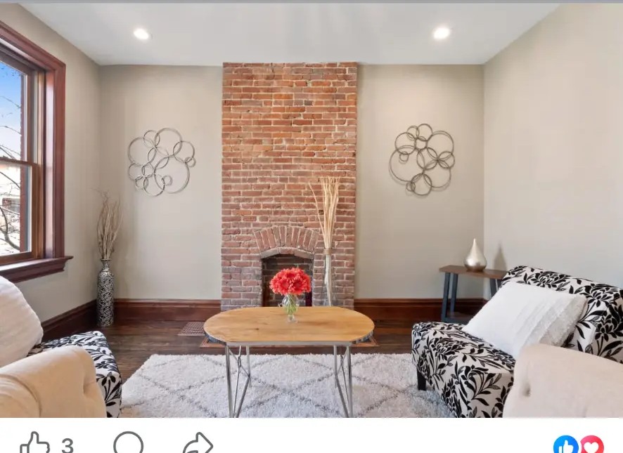 Living room with exposed brick fireplace, patterned armchairs and round wood coffee table