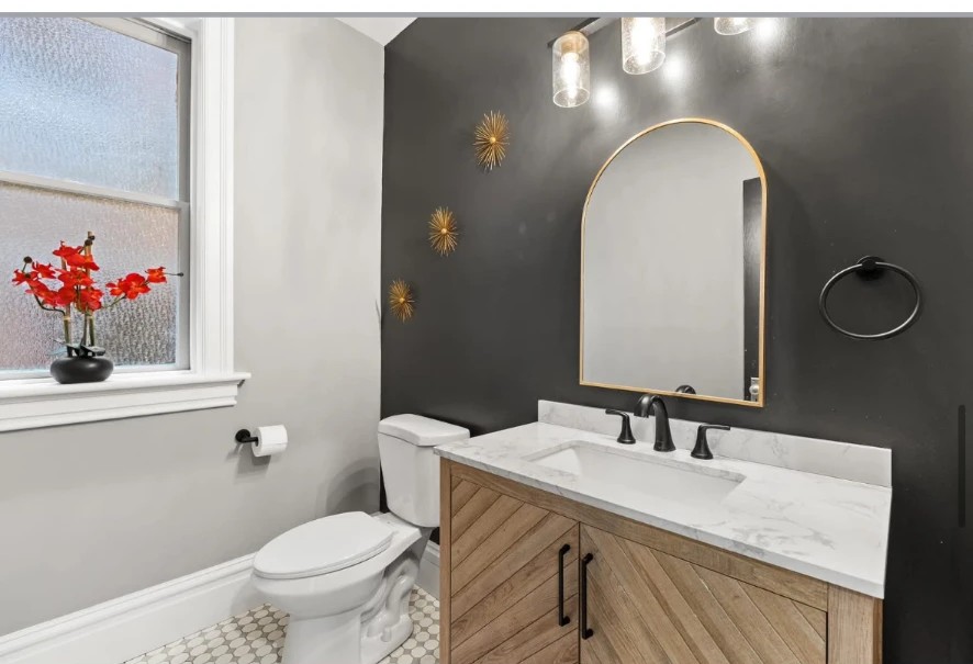 Bathroom with herringbone wood vanity, arched mirror and dark accent wall with gold sconces
