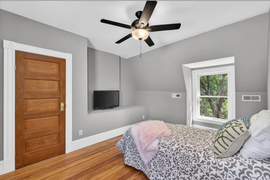 Bedroom with wood paneled door, ceiling fan, wall-mounted TV and patterned bedding