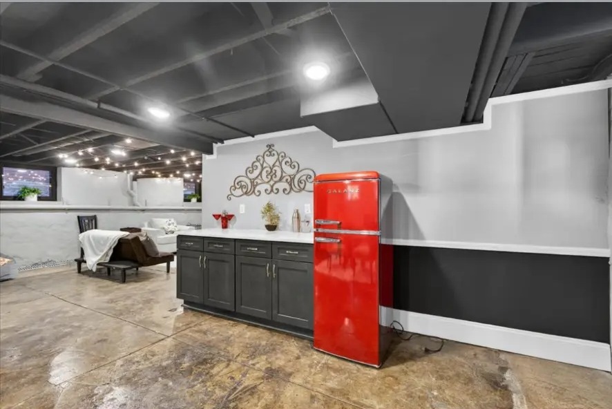 Dark base cabinets, red retro refrigerator and white-painted walls in a finished basement
