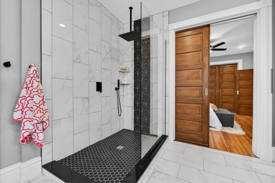 Glass walk-in shower with marble-look wall tile, black hexagonal floor tile and black fixtures
