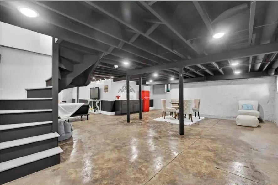 Finished basement with painted open ceiling, black stair treads and polished concrete floor