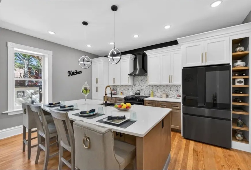 Kitchen with white upper cabinets, wood island, black refrigerator and patterned backsplash