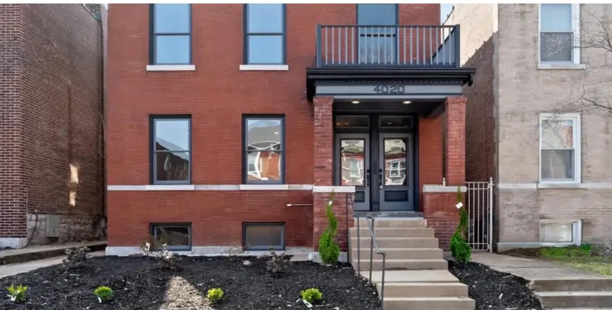 Red brick home with black-trimmed windows, double entry doors and an upper balcony