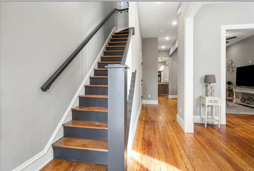Wood staircase with dark handrail beside a hallway with hardwood floors and white trim