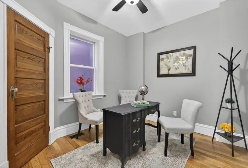Home office with black writing desk, upholstered chairs, wood door and tall window