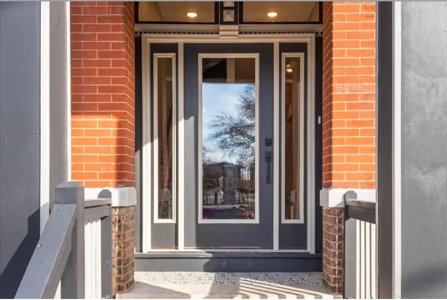 Front entry with full-glass door, sidelights, red brick porch columns and white railings