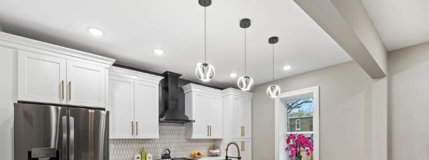 Kitchen with white cabinets, black range hood, hexagonal tile backsplash and glass pendant lights