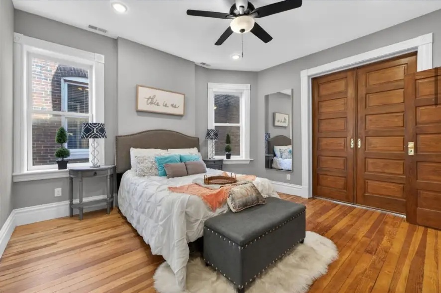 Bedroom with paneled wood closet doors, upholstered bed and bench, and white window trim