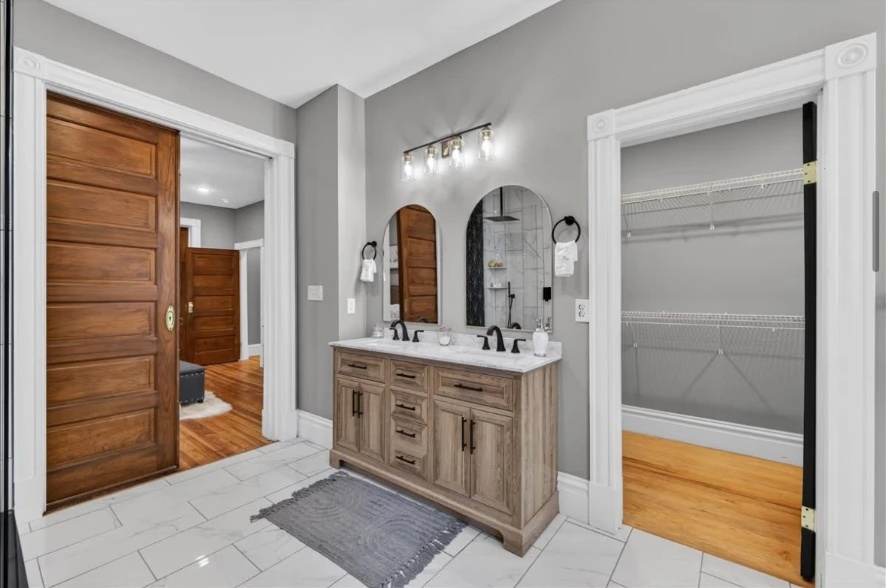 Wood double vanity with black faucets and two arched mirrors beside an open closet