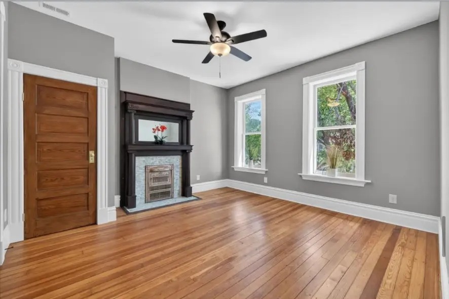 Bedroom with wood door, dark fireplace mantel, ceiling fan and hardwood floors