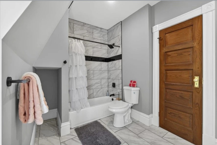 Bathroom with tiled tub surround, black fixtures, toilet and wood paneled door
