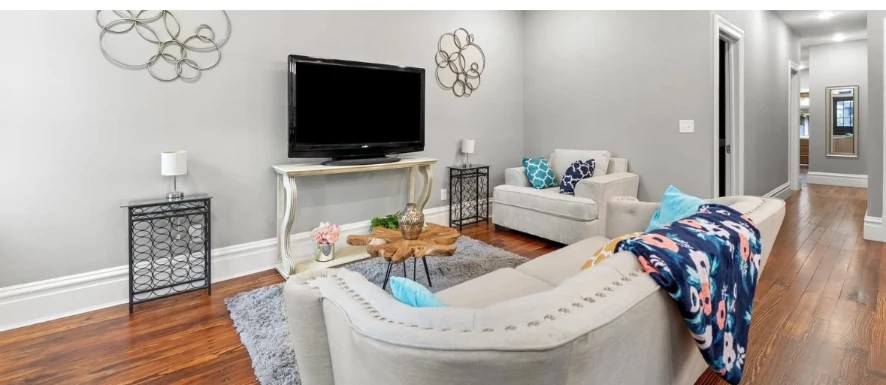 Living room with curved sofa, TV console, hardwood floors and hallway view
