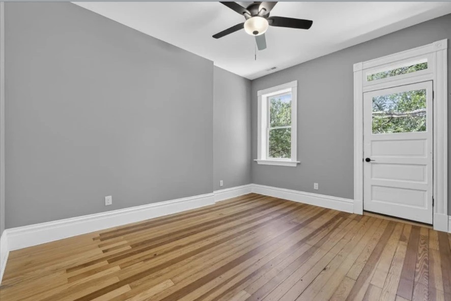 Empty gray room with ceiling fan, hardwood floors and white glazed door