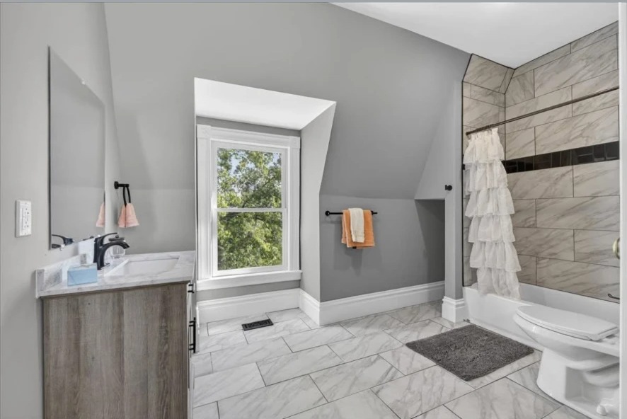 Attic bathroom with dormer window, gray vanity, tiled tub surround and white tile floor