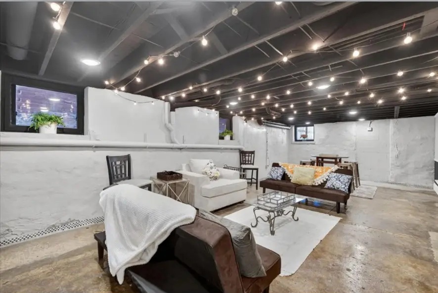 Basement lounge with string lights across a black ceiling, sofas and glass coffee table
