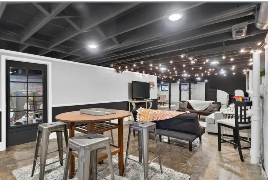 Finished basement with round dining table, metal stools, string lights and seating area