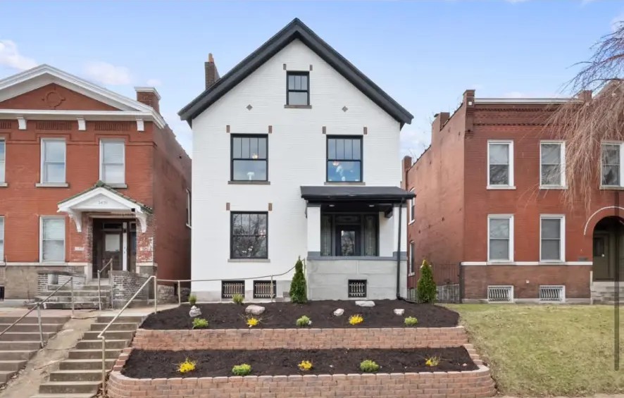 White painted brick home with black trim, terraced brick landscaping and covered porch