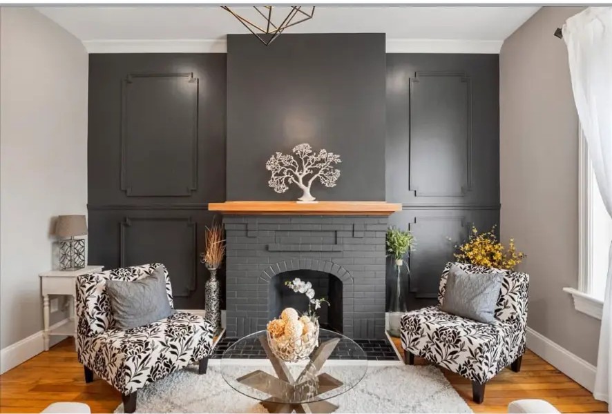 Living room with dark paneled feature wall, brick fireplace, wood mantel and patterned armchairs