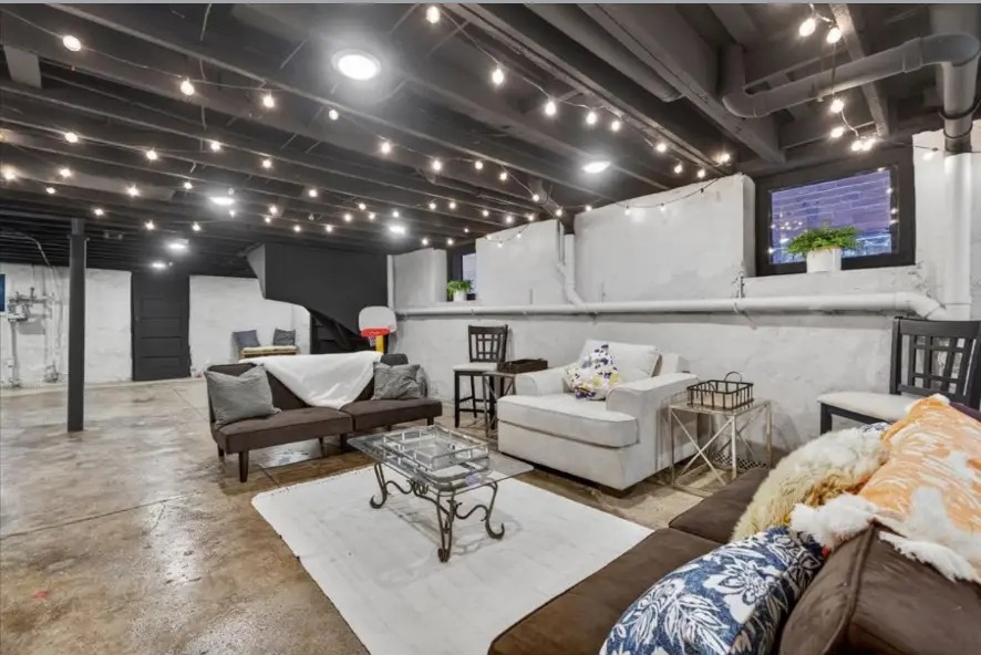Basement lounge with sofas, glass coffee table, white rug and stained concrete floor